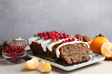 Tasty Christmas cake with icing, cranberries, nuts, tangerines and festive decor on light grey table, closeup