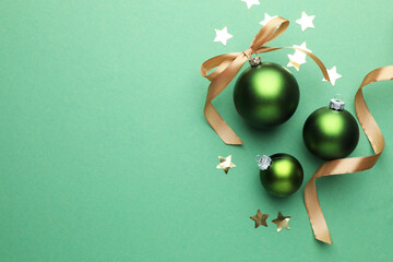 Beautiful Christmas composition with baubles, golden ribbon and confetti on green background, flat lay. Space for text