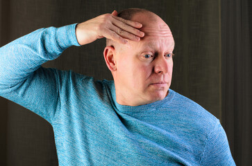 A bald man in a blue sweater is shielding his eyes, perhaps from the sun or deep in thought