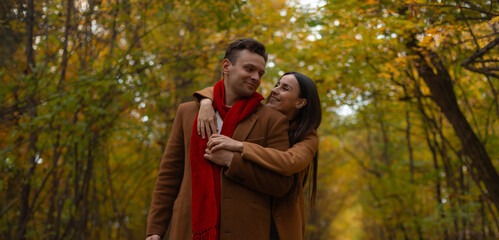 Happy couple in brown coats embracing in autumn park, smiling and looking at each other with love, surrounded by golden foliage and warm seasonal colors of fall.