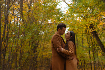 Romantic couple embracing in an autumn forest, looking into each other’s eyes. Warm, intimate moment perfect for Valentine’s Day, love, and relationship themes.