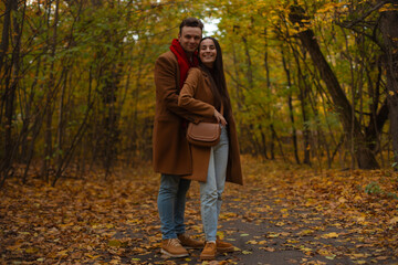 Happy couple hugging in an autumn forest, dressed in warm coats and enjoying a romantic walk. Cozy fall atmosphere, perfect for Valentine’s Day, love, and relationship themes.