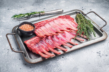 Raw mutton meat for chops steaks, uncooked rack of lamb on steel tray with herbs. grey background. top view