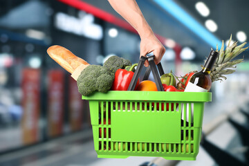 Customer holding shopping basket with different food products at supermarket, closeup