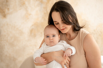 a mother holds a newborn baby in her arms, a mother gently hugs and kisses a small child, maternal love and care, a mom and a baby