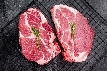 Raw pork tender steak, fresh neck meat with herbs on steel rack. black background. top view