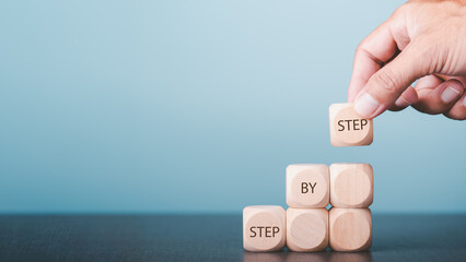 Hands arrange wooden blocks stacked into steps and display messages Step By Step. Business ideas for ladder of personal success, success and growth.