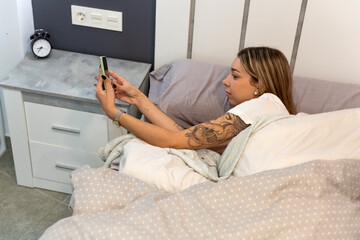 Obraz premium Young woman checking smartphone in bed