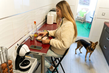 Young woman enjoying breakfast with dog in kitchen
