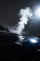 Automotive service technician inspecting vehicle with steam rising in a workshop at night