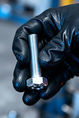 Worker holds a shiny hex bolt in a busy automotive service shop during a maintenance task