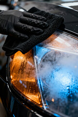 Vehicle headlight cleaning service in an automotive workshop with steam and water droplets visible