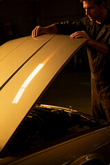 Automotive technician working on car in dimly lit garage during evening