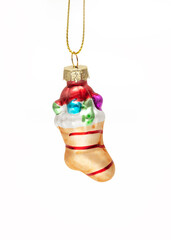 A decorative glass Christmas stocking ornament, filled with small, colorful gifts and candy, hanging on a gold cord against a clean white backdrop