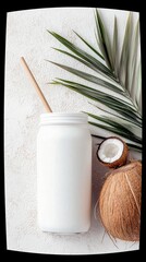 A white mason jar filled with coconut milk, a wooden straw, a whole coconut, a halved coconut, and a palm leaf on a textured white surface.