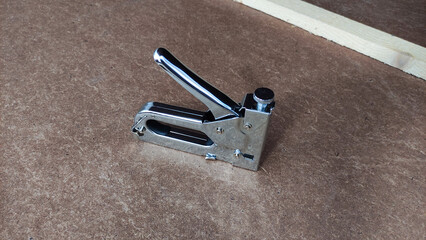 Shiny metal staple gun resting on brown textured work surface, highlighting DIY tools and home improvement materials.