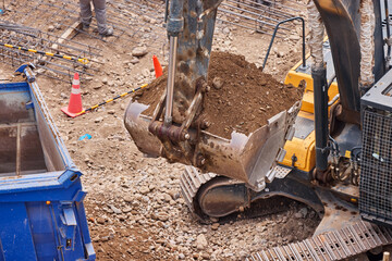 An excavator bucket releases a heavy load of soil into the truck bed, powering the steady rhythm of progress on the construction site.
