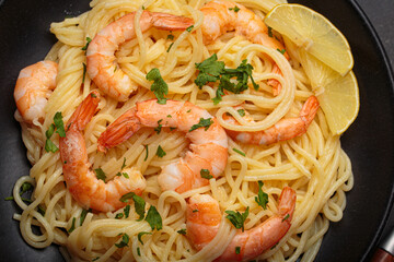 Cooked spaghetti with prawns shrimps, fresh parsley, and wedges of lemon on a black plate, ready for serving