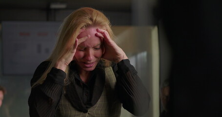 Blonde businesswoman struggling with emotional distress in office, holding head and clenching fists...
