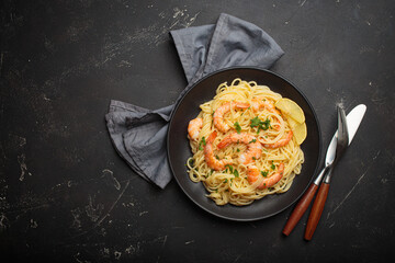 Cooked spaghetti with prawns shrimps, fresh parsley, and wedges of lemon on a black plate, ready for serving space for text
