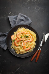 Cooked spaghetti with prawns shrimps, fresh parsley, and wedges of lemon on a black plate, ready for serving