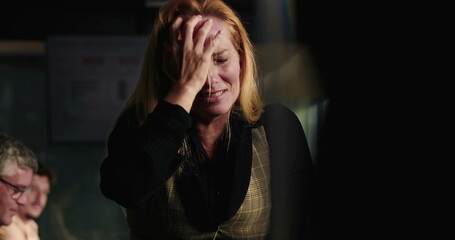 Blonde businesswoman in visible emotional breakdown during office meeting, holding head with both hands under intense stress and pressure at work