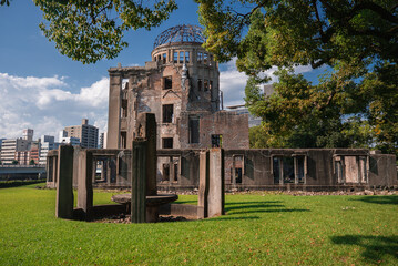 Hiroshima Peace Memorial in Hiroshima, Japan shows the preserved dome and ruins, a circular stone installation with pillars, open lawn, and city buildings beyond.