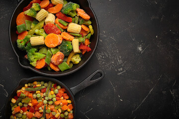 Preparing healthy meal with vibrant frozen mixed vegetables in cast iron pans on a dark background, top view space for text