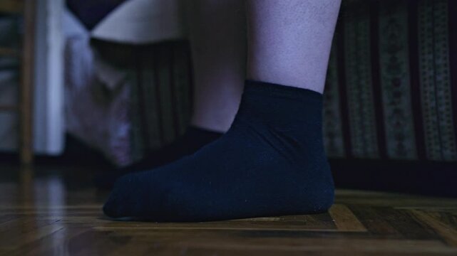 Close-up of a person's feet in black socks on a beautiful wooden parquet floor, gently stretching. The subtle movements convey a sense of comfort and a relaxed start or end to the day indoors.