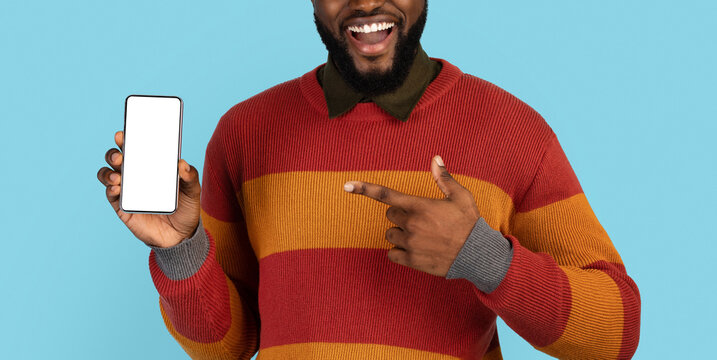 Smiling Black Man Pointing At Blank Cellphone With White Screen In His Hand, Happy Excited Young African American Male Recommending New Mobile App Or Website, Cropped Shot, Panorama, Mockup