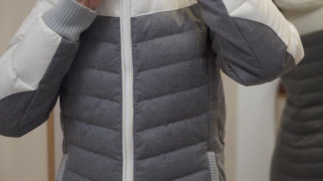 Plastic zipper teeth on a cloth puffer jacket are pulled down quickly by a person's hand. The action creates a metallic, high-pitched zzzzip sound.