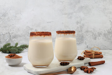 Eggnog with cinnamon, star anise, and nutmeg for Christmas and the winter holidays on a marble table with fir branches. A warming eggnog during the cold season, a festive arrangement for Christmas Eve