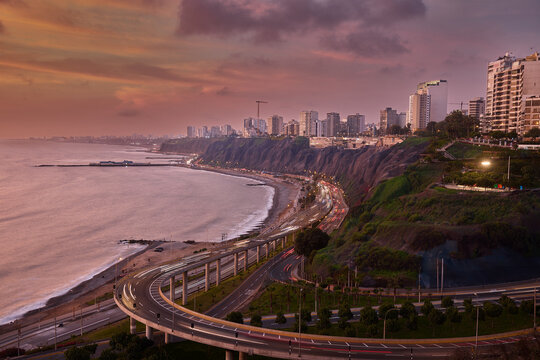 Night view of Miraflores with light trails, coastal highway, and city lights reflecting over the Pacific.
