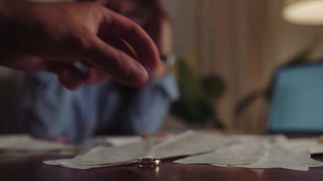 Depressed young couple arguing while checking their financial debt. The husband takes off his wedding ring and throws it on the table where there are piles of bills for debts. High quality 4k footage