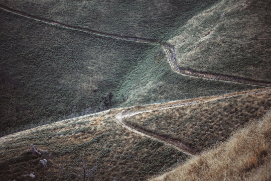Telephoto winter view of winding hillside paths cutting through textured grass and scrub in Asturias, forming organic geometric lines and a rugged, remote Camino de Santiago landscape - Powered by Adobe