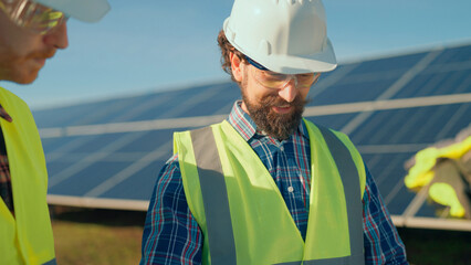 Workers assess solar panels under clear blue sky on a bright day while wearing safety gear and discussing project details