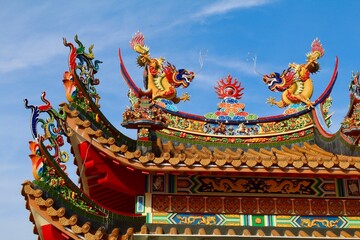Fototapeta premium Traditional Chinese Temple Architecture with Colorful Dragons and Decorative Roof Sculptures Under Clear Sky, Detailed Asian Cultural Artwork and Ornamental Heritage Design