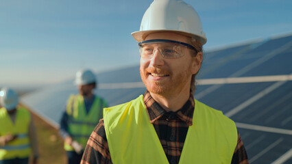 Workers install solar panels at a renewable energy site while wearing safety gear on a sunny day