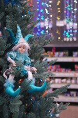 Vintage elf figurine in blue suit on artificial Christmas tree on the background of shelves with toys and colorful garlands out of focus as a new year gift shopping concept