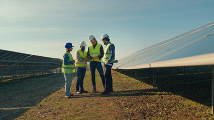 Workers discuss solar panel installation at a renewable energy site in bright afternoon sunlight