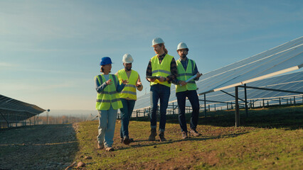 Team of solar energy workers inspecting panels at a renewable energy site during a sunny day in the countryside