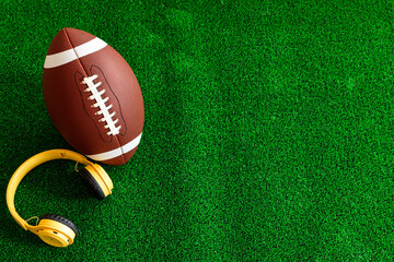 Football is laying on the grass next to a pair of headphones