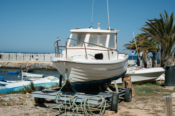 Fototapeta premium Vintage boat on trailer at sunny coastal harbor with palm trees