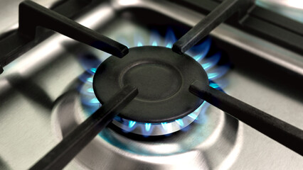 Close-up of a burning gas stove with blue flames on a stainless steel surface. Home kitchen background. Banner