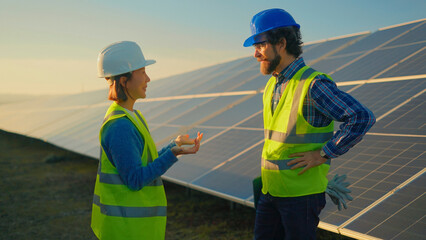 Workers discuss solar panel installation at a renewable energy site during sunset