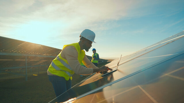 Workers install solar panels under the clear blue sky at a renewable energy site during the golden hour
