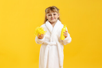 Happy girl in bathrobe with loofah and cosmetic product on yellow background