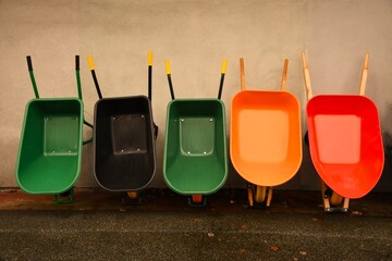 Five upright brand new colorful wheelbarrows leaning against grey wall. © tom