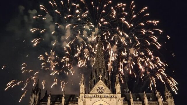 A spectacular display of golden fireworks illuminates the dark night sky, exploding in a dazzling finale above the spires of a historic gothic cathedral. This grand, festive scene evokes feelings of c