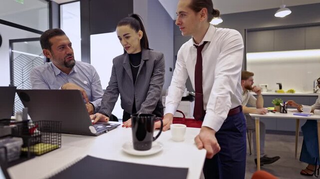 Engaged business colleagues work together, reviewing data on a laptop and exchanging thoughts. This dynamic team collaborates effectively in a contemporary office setting.